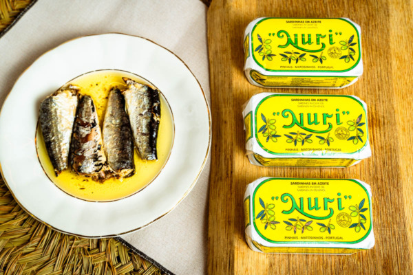 Lata de sardinas Nuri en aceite de oliva junto a un plato con sardinas